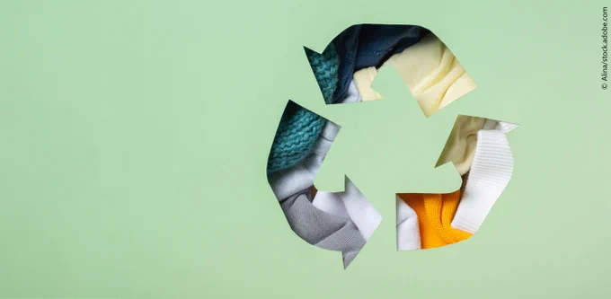 Colorful clothes under paper cut recycling symbol.