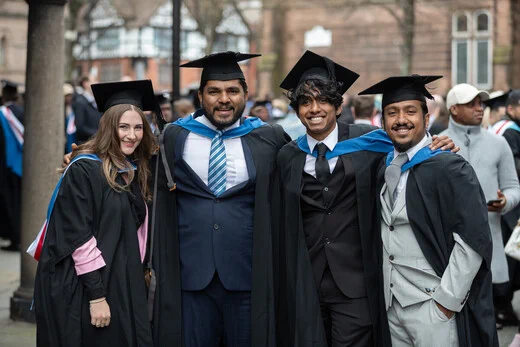 four graduates side by side, wearing caps and gowns smiling.