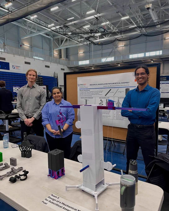 Three students standing behind a table with their capstone project on display. Their project poster is on a bulletin board behind them.