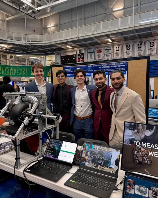 Five students standing behind a table that is displaying two laptops and various elements of their capstone project.