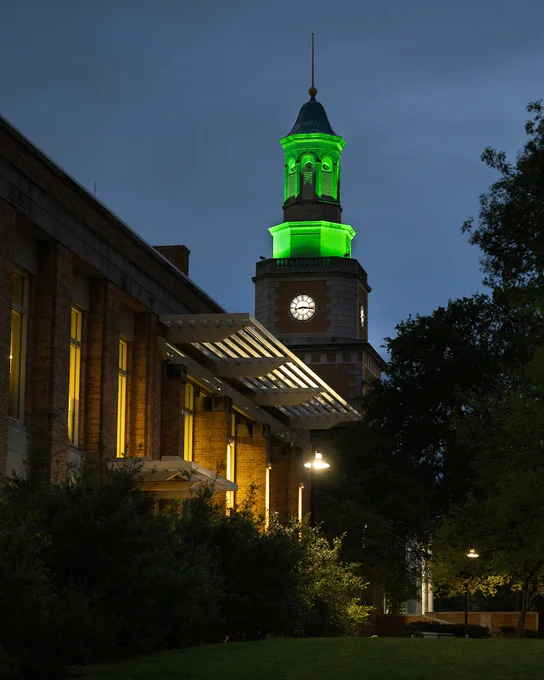 UNT's McConnell Tower lit green at dusk at Hurley Administration Building with the UNT Union in the foreground.