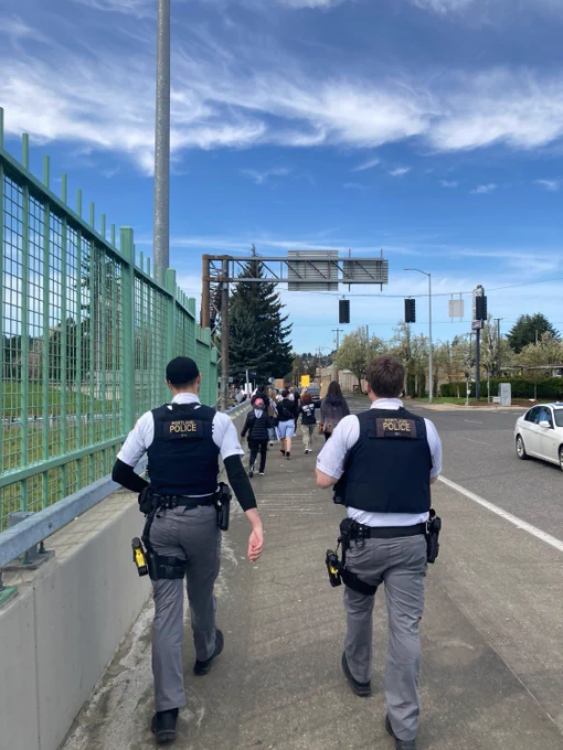 Two Dialogue Officers in white uniform shirts walk along outside of a march on the sidewalk