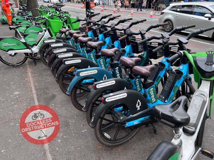 Rows of Forest bikes deployed on pavement for hire surrounded by lime bikes.