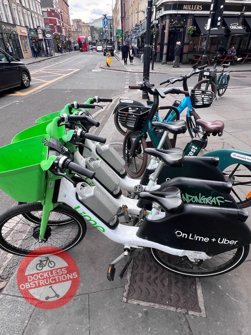 Six dockless hire ebikes left on pavement around a single public cycle parking rack outside Tesco Kings Cross Islington.