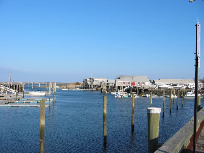 Photo of Barnstable Harbor with piers, buildings, water and boats.