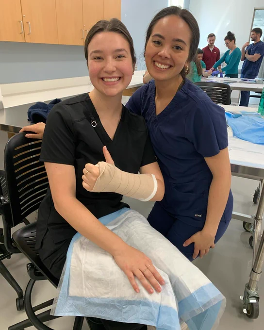Two physician assistant students smile at the camera during a simulation splinting lab activity.