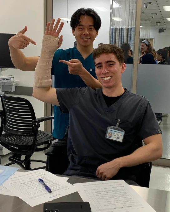 Two physician assistant program students smile at the camera during a simulation lab focused on arm splinting. 