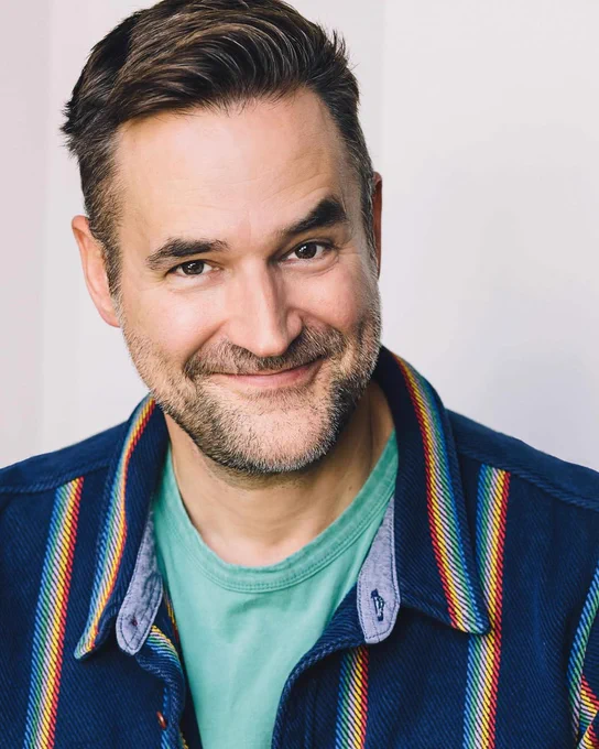Picture of Connor Barrett wearing a green shirt and a jacket with rainbow stripes.
