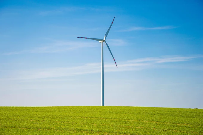 a single wind turbine on a grassy hill with a blue, nearly cloudless sky in the background.