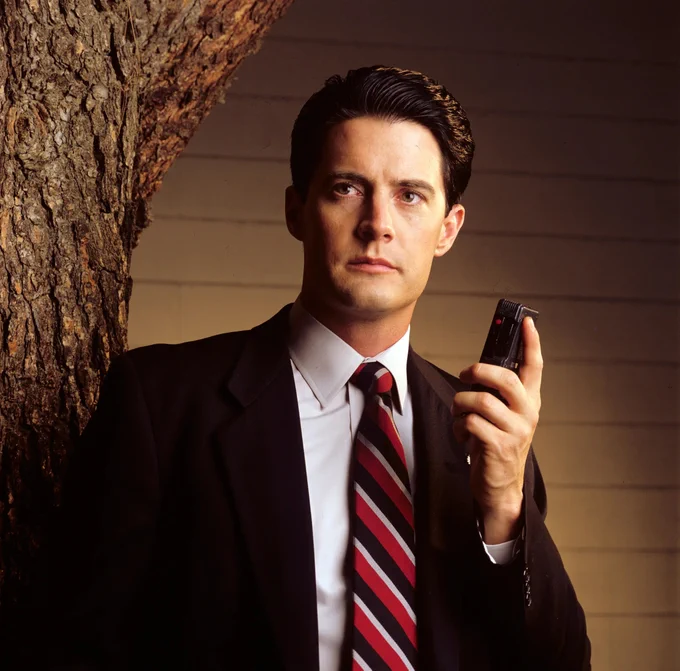 A man wearing a suit and a red striped tie, holding a voice recorder in his hand