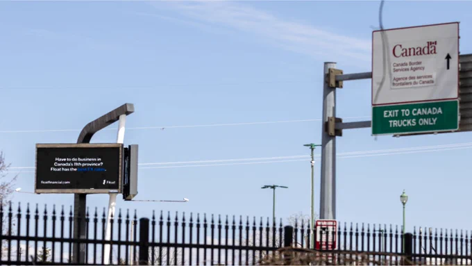 Road signs at a border crossing, including a "Canada Border Services Agency" sign, with an arrow directing "Exit to Canada Trucks Only.