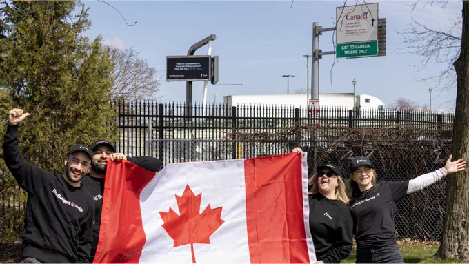 Group of people holding a Canadian flag and celebrating in front of a Canada Post facility.