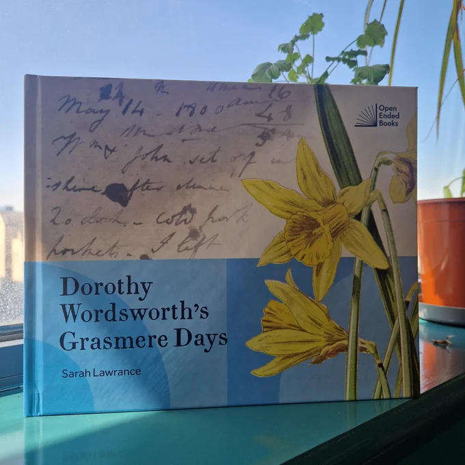 Photo of a blue book about Dorothy Wordsworth with a large daffodil on the cover next to handwriting in a journal