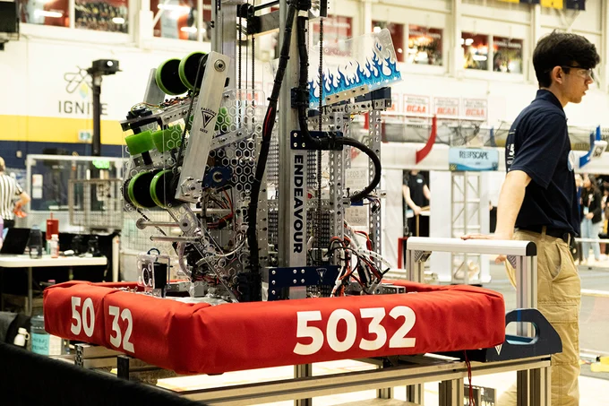 A person stands next to a robot with the number 5032 on its base.

