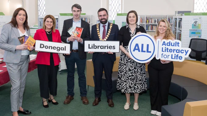 Six people standing side by side holding books and signs. 