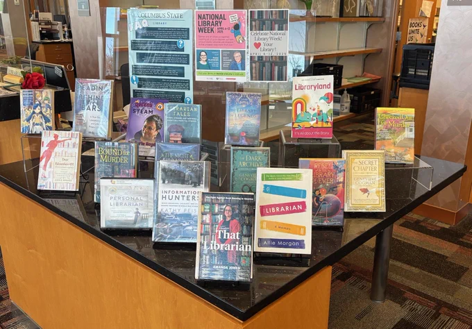 Tabletop book display featuring both fiction and non-fiction about libraries and librarians, with related signage.
