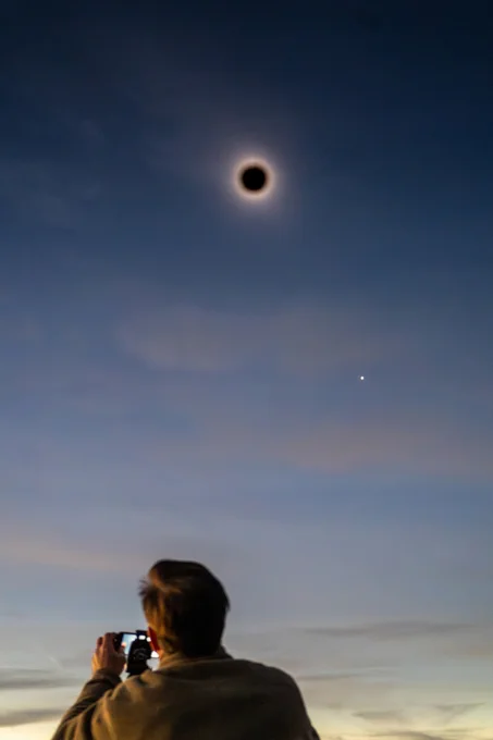An individual capturing a photo of a total solar eclipse in a twilight sky.