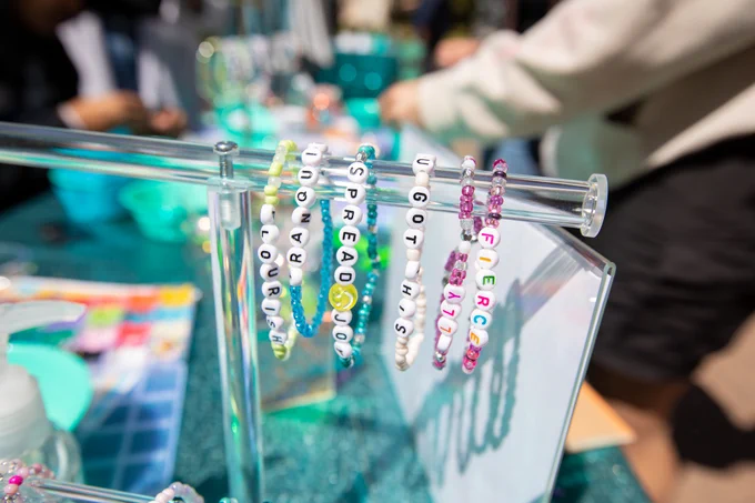 Colorful beaded bracelets with inspirational words displayed on a clear stand at an outdoor event.