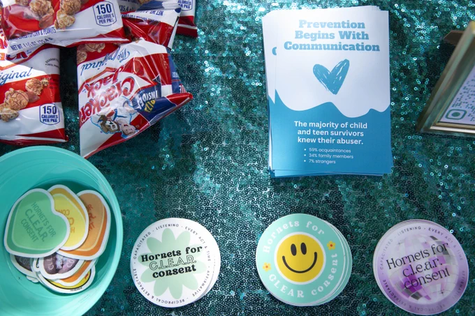 Promotional materials and snacks including pamphlets, buttons with messages advocating for clear consent. They are arranged on a blue glittery background.