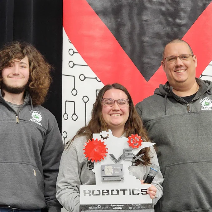 A student smiles proudly and holds up an impressive custom trophy shaped like the state of Minnesota.