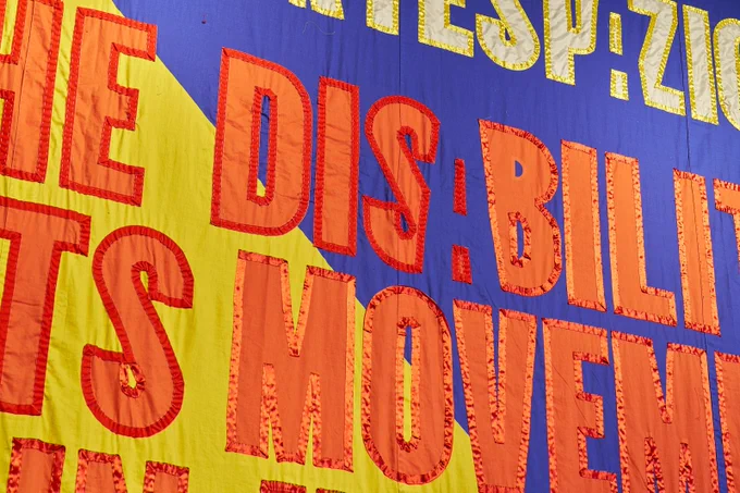 A close up of a giant, colourful banner says 'The Disability Arts Movement'.
