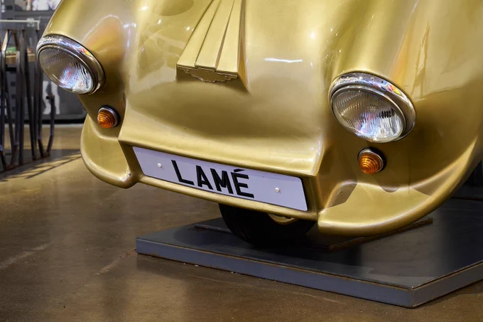 The front of a golden car with the number plate saying 'LAME'.