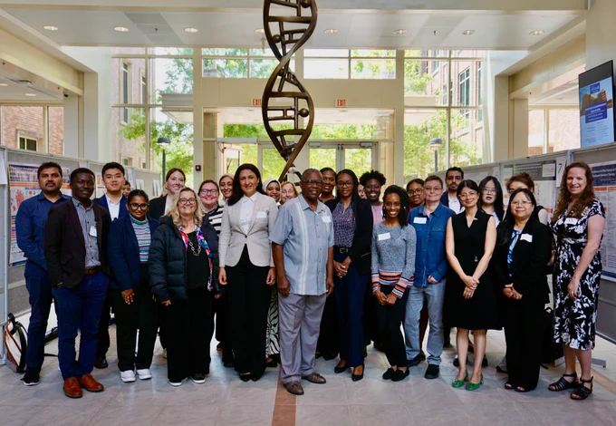 A group of people poses for a photo in the atrium of the Cancer Center in front of a DNA helix statue.