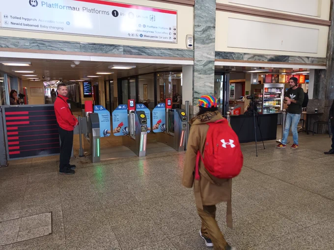 An individual is being filmed walking towards the ticket barriers in Cardiff Central Station.