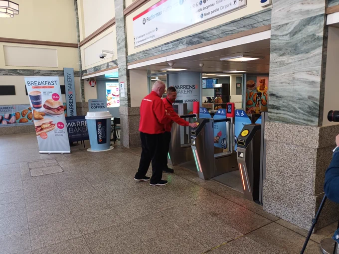 A member of staff from Cardiff Central Station helps an individual get through the ticket barriers.