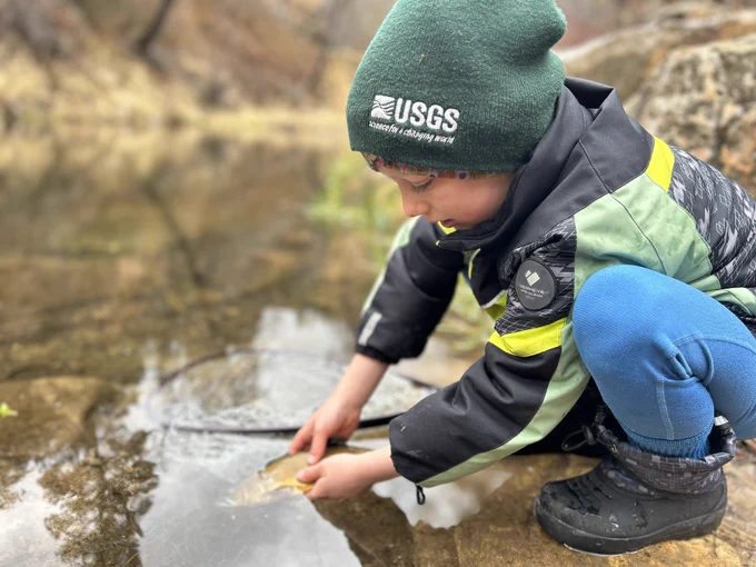 USGS biologist and Safety Program Coordinator Morgan Ford's son, wearing a USGS cap "because Dad wears one", gently releases a Gila trout from the banks of a calm stream during fishing in northern Arizona. Photo courtesy of Morgan Ford, USGS Southwest Biological Science Center.