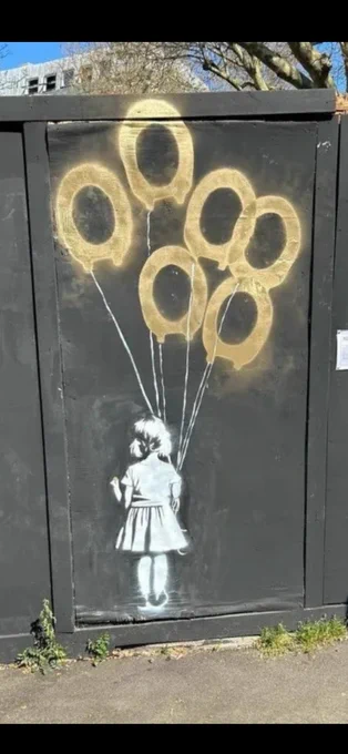 A stencilled image of a little girl with her back facing the viewer is in white and spray painted on a black background . The girl is holding golden balloons that are in the shape of toilet seats.