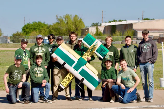 A group of students gathered around a model plane.