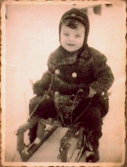 A boy in winter clothes and a hat is sitting on a sledge. He is photographed slightly from above.
