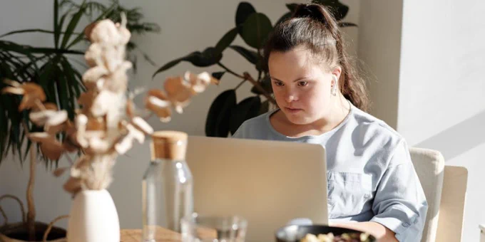 Young woman with Down syndrome using a laptop at a cozy home setting, enjoying leisure time.