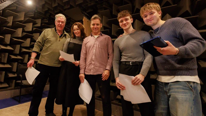 5 members of The Archers cast stood holding their paper scripts in a group shot taken inside the recording studio