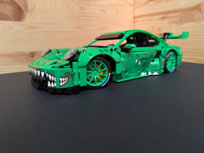 A brick built (not Lego) Porsche 911 GT3-R with the "Rexy" livery, kind of depicting a T-Rex. Shown from the front left.