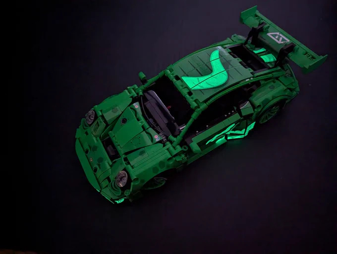 A brick built (not Lego) Porsche 911 GT3-R with the "Rexy" livery, kind of depicting a T-Rex. Shown from the top, in the dark, to show off the glow in the dark stickers. Teeth, claws and part of the body are glowing!