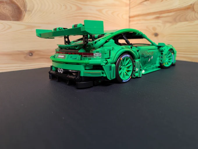 A brick built (not Lego) Porsche 911 GT3-R with the "Rexy" livery, kind of depicting a T-Rex. Shown from the rear right.