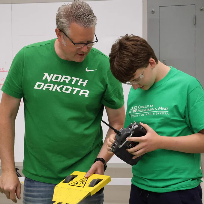 A UND faculty member holds a kid's robot as they help mentor the student on how the robot works.