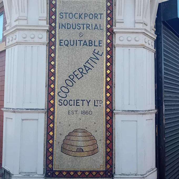 The mosaic reads: "Stockport Industrial & Equitable Co-operative Society Ltd, Est. 1860" with the word "Co-operative" arranged diagonally across the middle. At the bottom is a classic beehive symbol, often associated with co-operatives, framed by a patterned border.