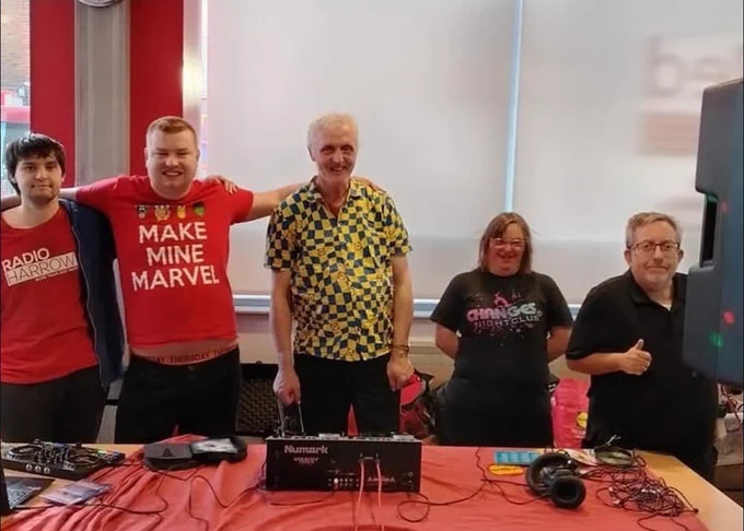 Five individuals stand around a table, collaborating and reviewing information displayed on a laptop.