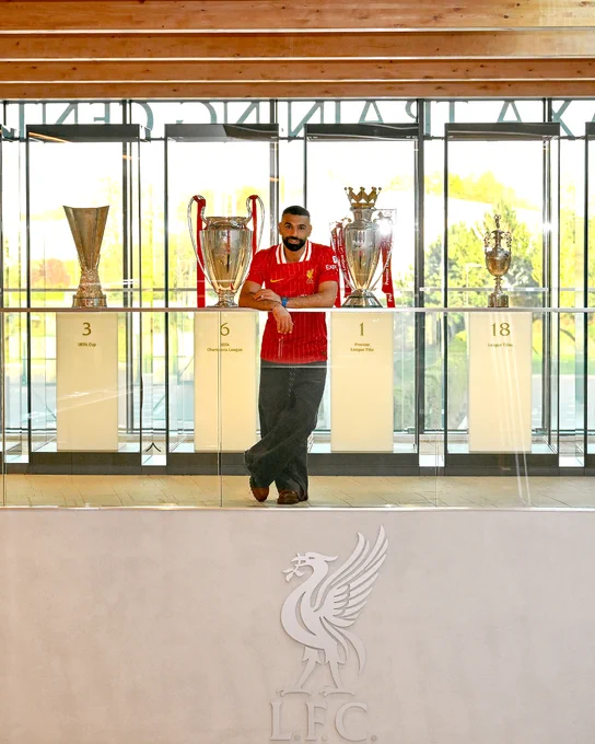 A photo of Mo Salah in front of the trophy cabinet at the AXA Training Centre
