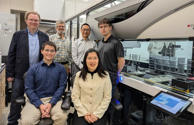 A group of six people next to robotic equipment in a lab