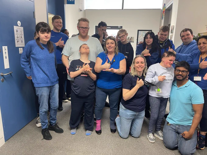 A large group of people of varying ages all dressed in blue clothes smiling and doing thumbs up to the camera. 