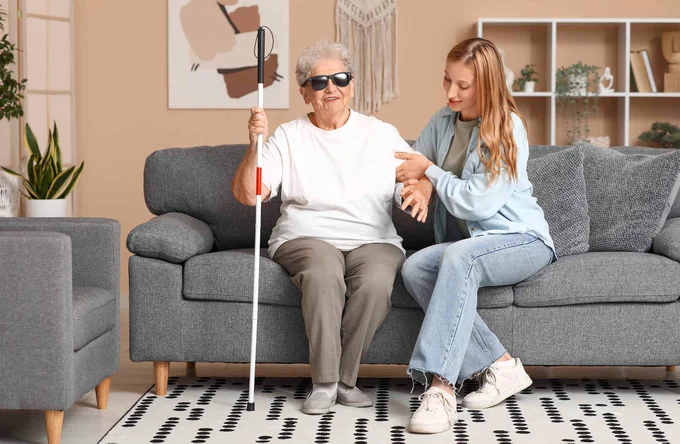 Woman with a visual impairment getting help to stand from seating position. Adobe stock