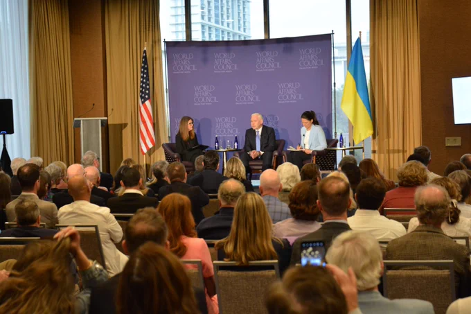 Krys, Ihor, and Olga sitting on stage with the American and Ukrainian flags around them