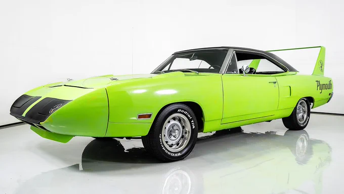 A Limelight green 1970 Plymouth Superbird is displayed in a studio setting. The car features distinctive aerodynamic design elements, including a tall rear spoiler and a pointed front end. The background is plain white, emphasizing the vehicle's vibrant color and design.