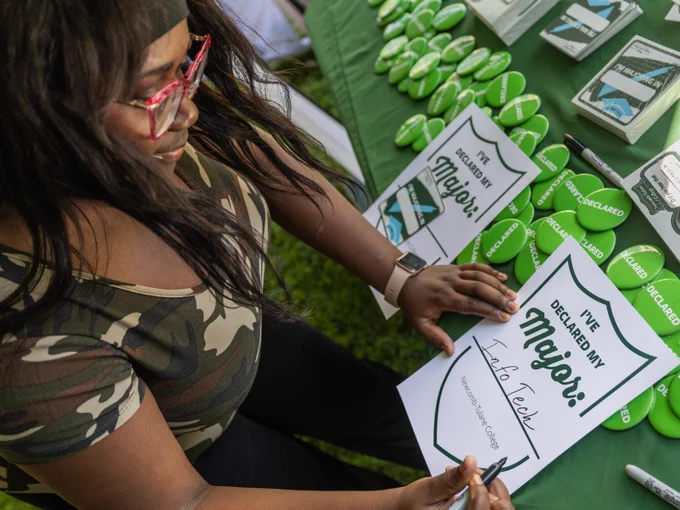 Person at a promotional event for "Declare Your Major", writing on paper with various Tulane branded materials visible on the table.