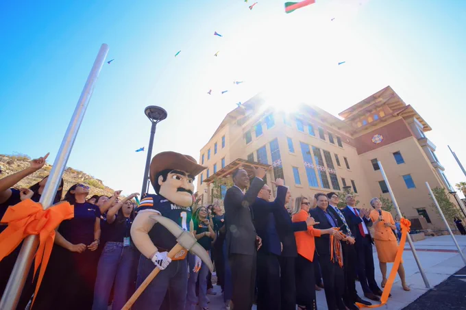 Group of people participating in a ribbon-cutting ceremony outside UTEP's new Advanced Manufacturing and Aerospace Center, with toy rockets flying in the air. UTEP mascot Paydirt Pete is visible to the left.