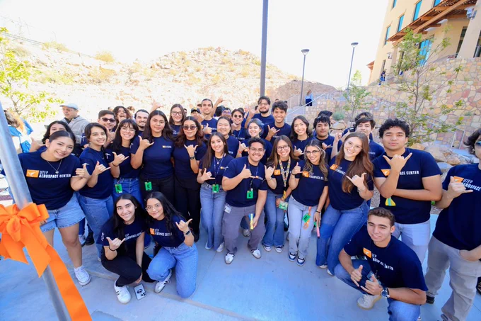 A group of students wearing UTEP Miners T-shirts, smiling and posing with the "picks up" hand sign, at the Advanced Manufacturing and Aerospace Center grand opening.